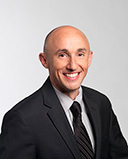 Smiling bald professional in dark suit and tie against light gray background