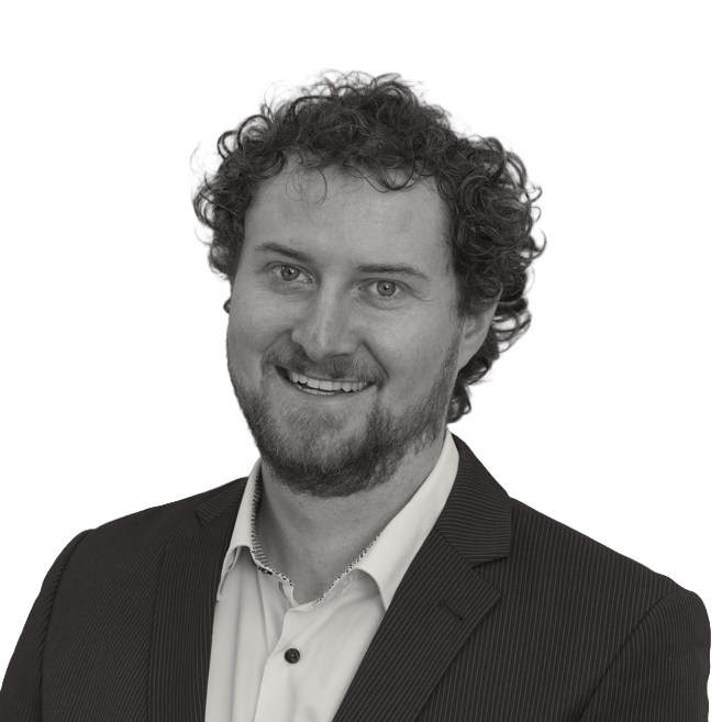 Headshot of Aurel Tscharner smiling, with curly hair and a beard, wearing a blazer and collared shirt