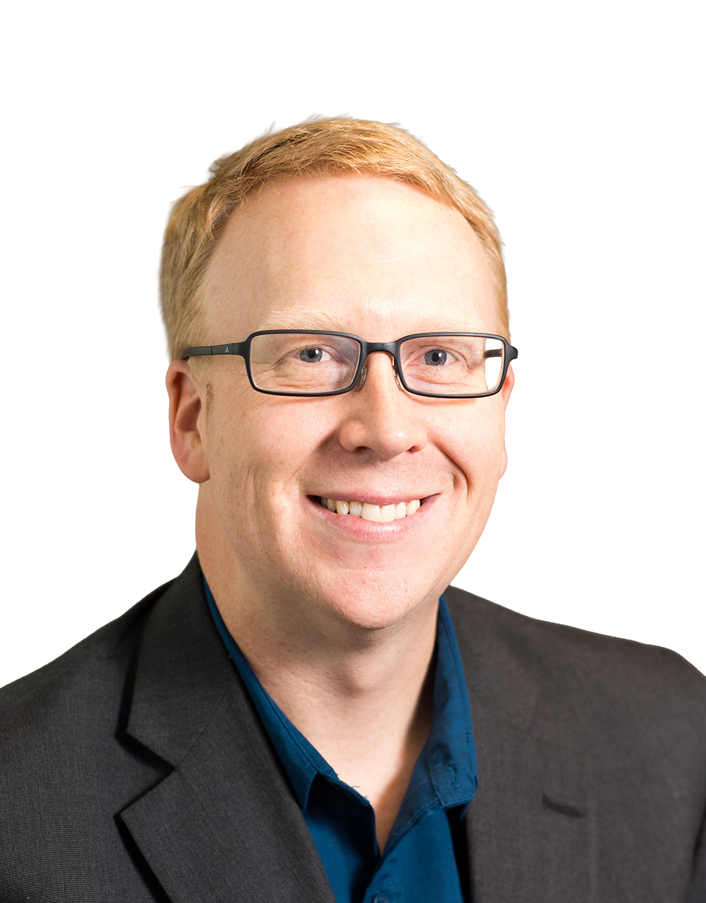 Smiling person with short red hair and dark-framed glasses, wearing a blue shirt and dark blazer