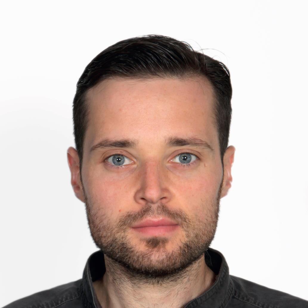 Headshot of a person with dark hair and blue eyes, wearing a dark collar shirt