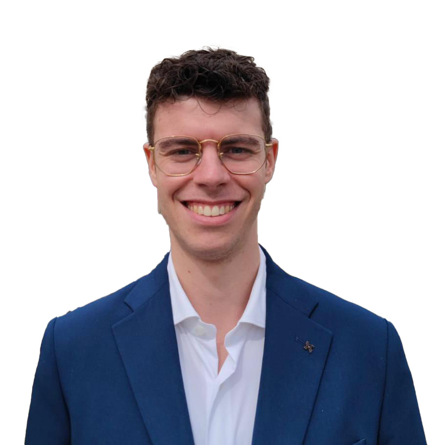 Smiling person with curly dark hair and gold-framed glasses, wearing a blue blazer over a white shirt